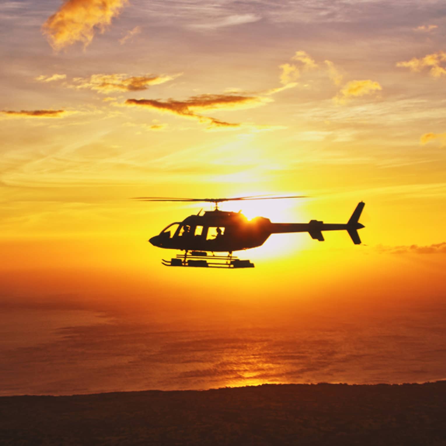 Silhouette of helicopter against orange sunset