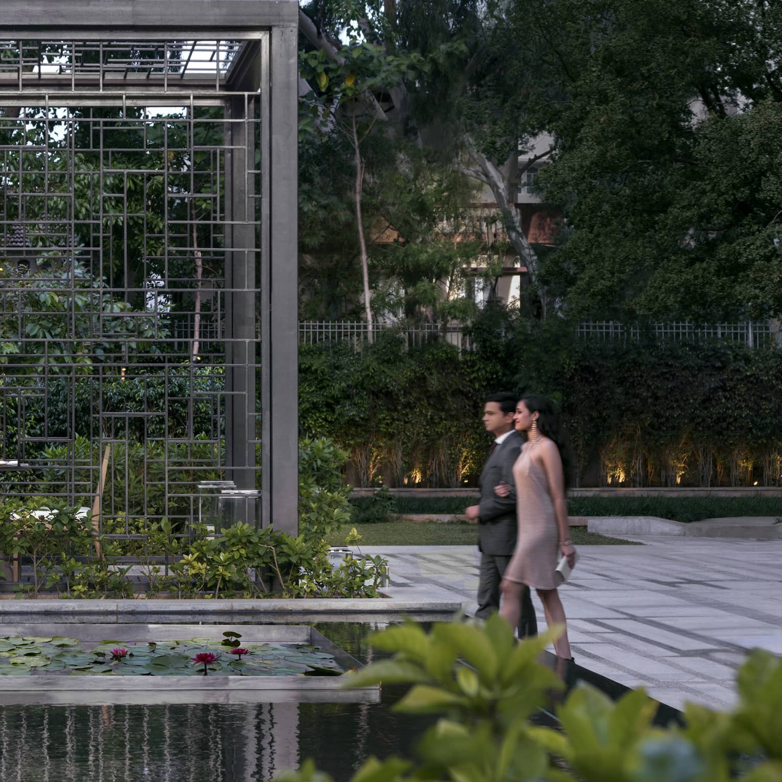 A couple walks through a dining area in a garden with lily pads and a waterfall