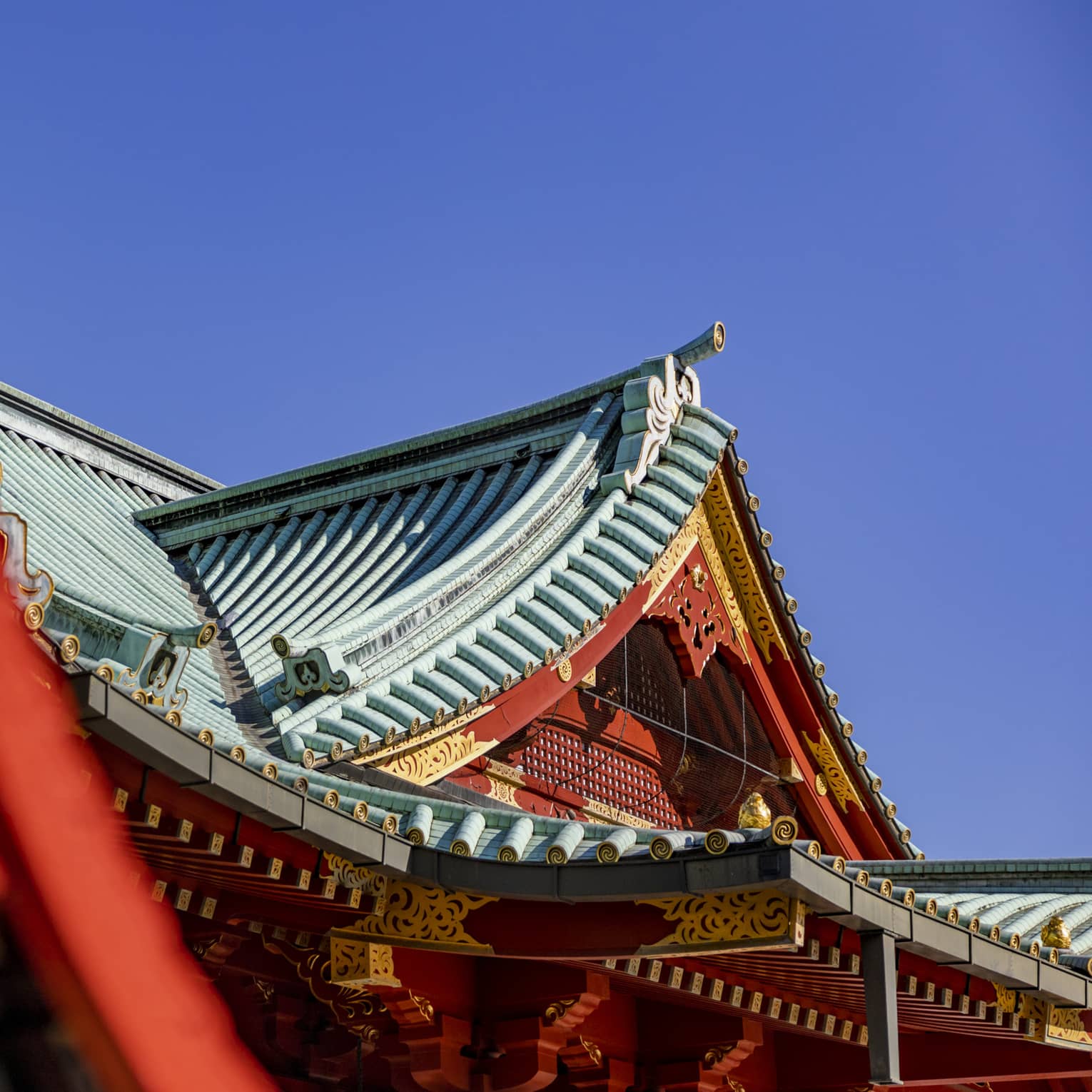 Concave tented gable rooftops of Shinto temples with ornate red and gold facades and grooved piping on the roofs.
