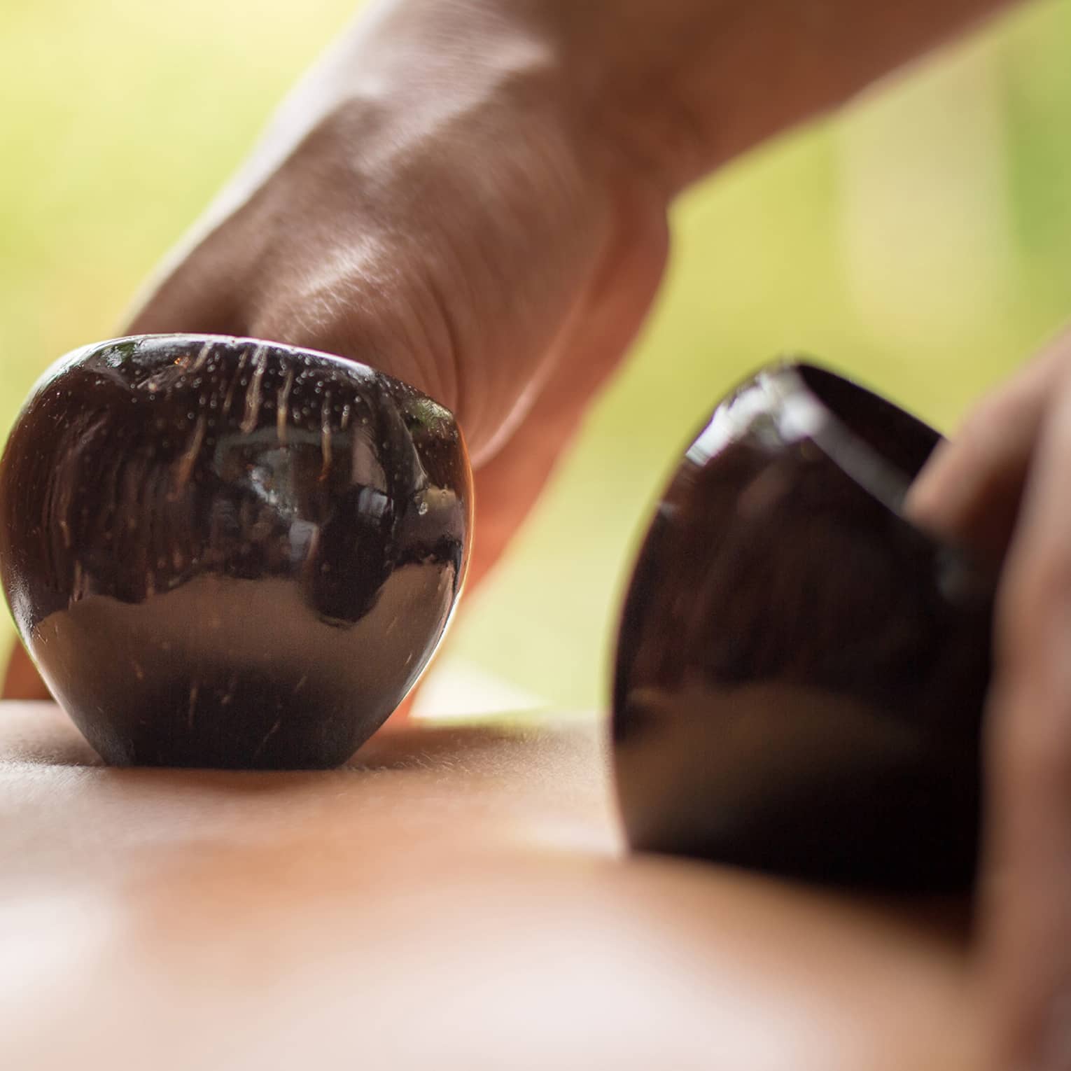 Close-up of hands massaging bare back with black coconut shells
