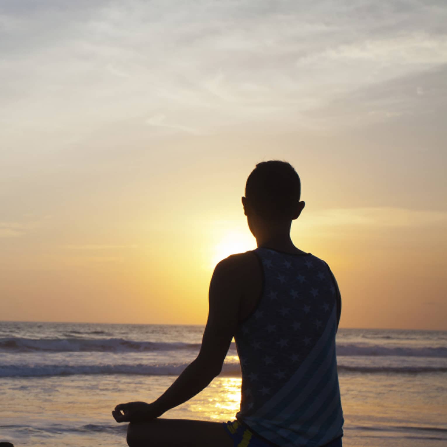 Silhouette of person sitting cross-legged, meditating in front of beach at sunset