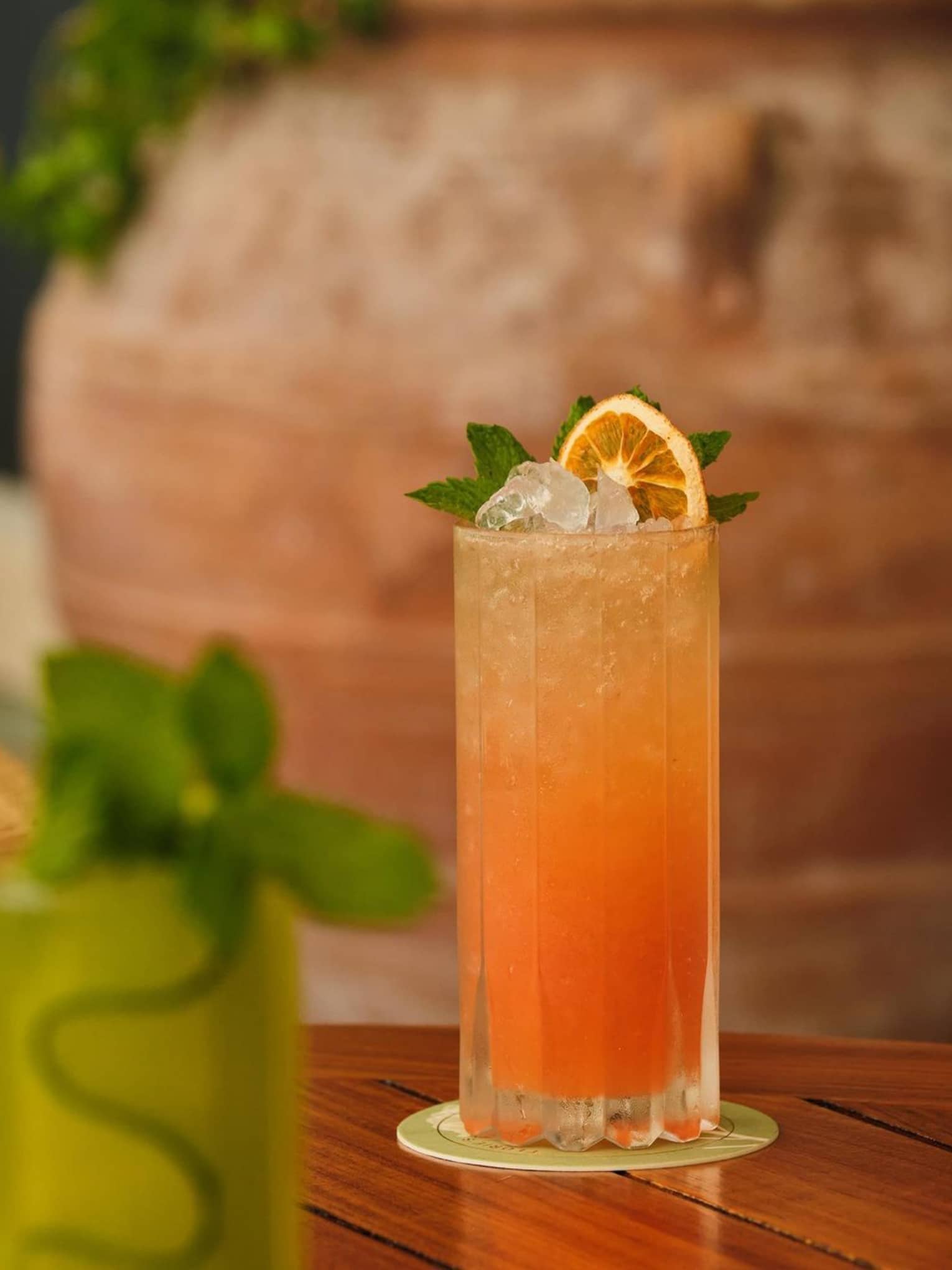 Orange-coloured cocktail served in a highball glass and garnished with an orange wheel and sprig of mint
