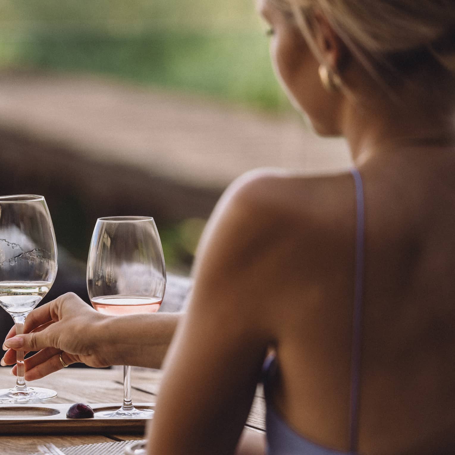 Person sitting at an outdoor table reaching for one of three wine glasses.