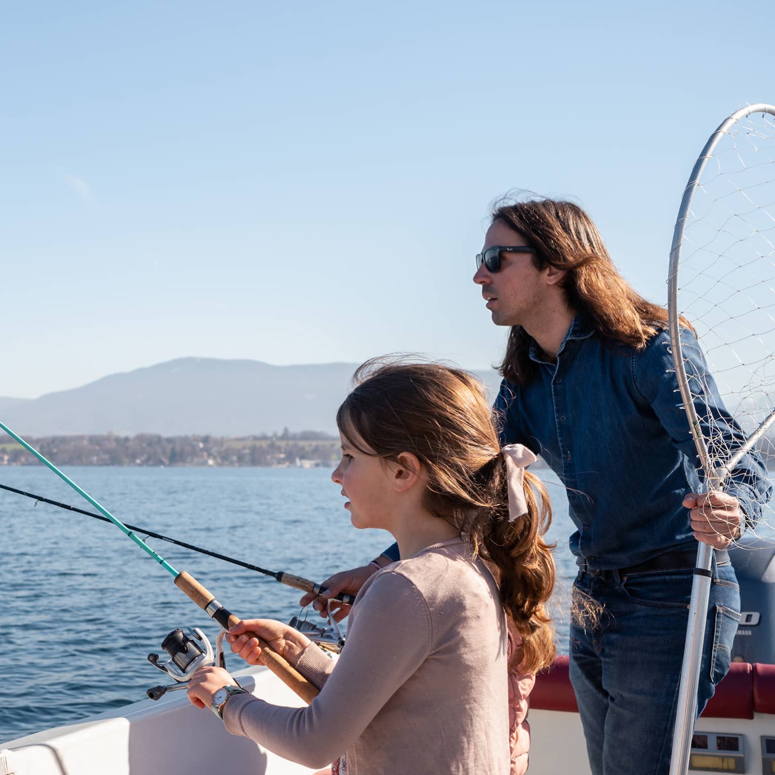 Man holding net and fishing rod, and girl standing in boat, holding fishing rod