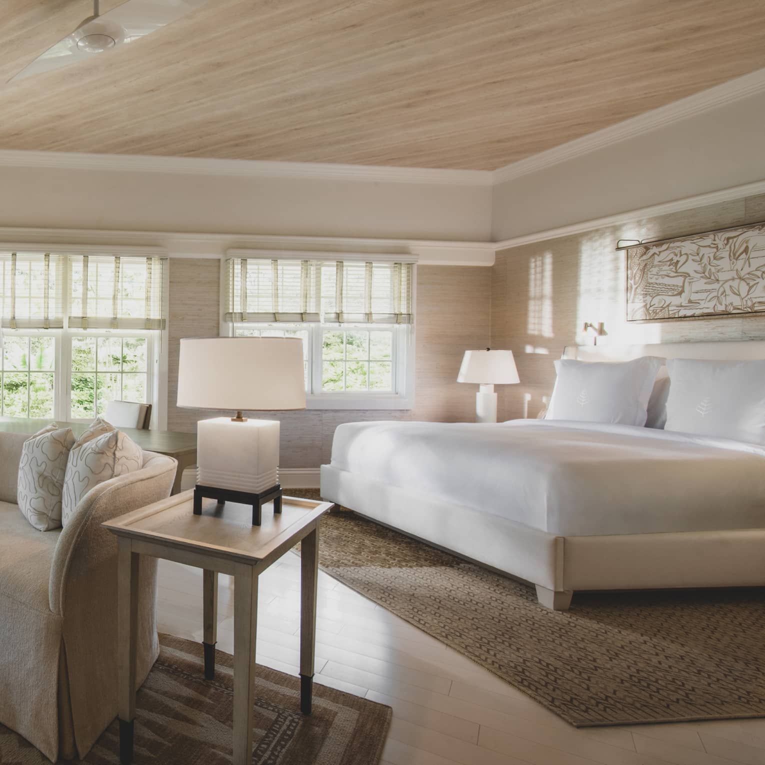 A vast room in whites and neutral tones, with abundant floor-to-ceiling windows and wood, and a luxurious king-sized bed.