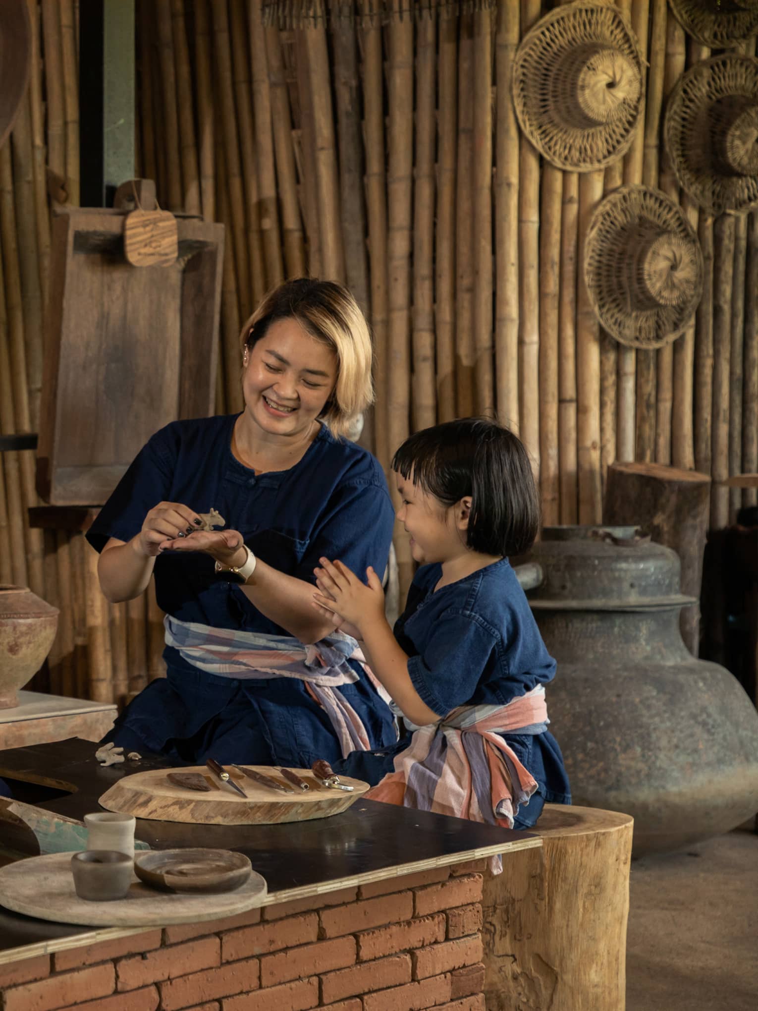 A potter teaching a woman and a child to shape clay in a rustic pottery workshop, surrounded by traditional tools and pottery.