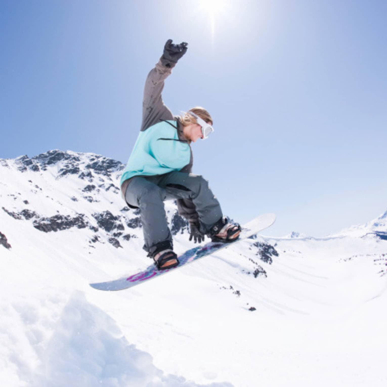 Snowboarder jumps, grabs board in mid-air on sunny mountain peak