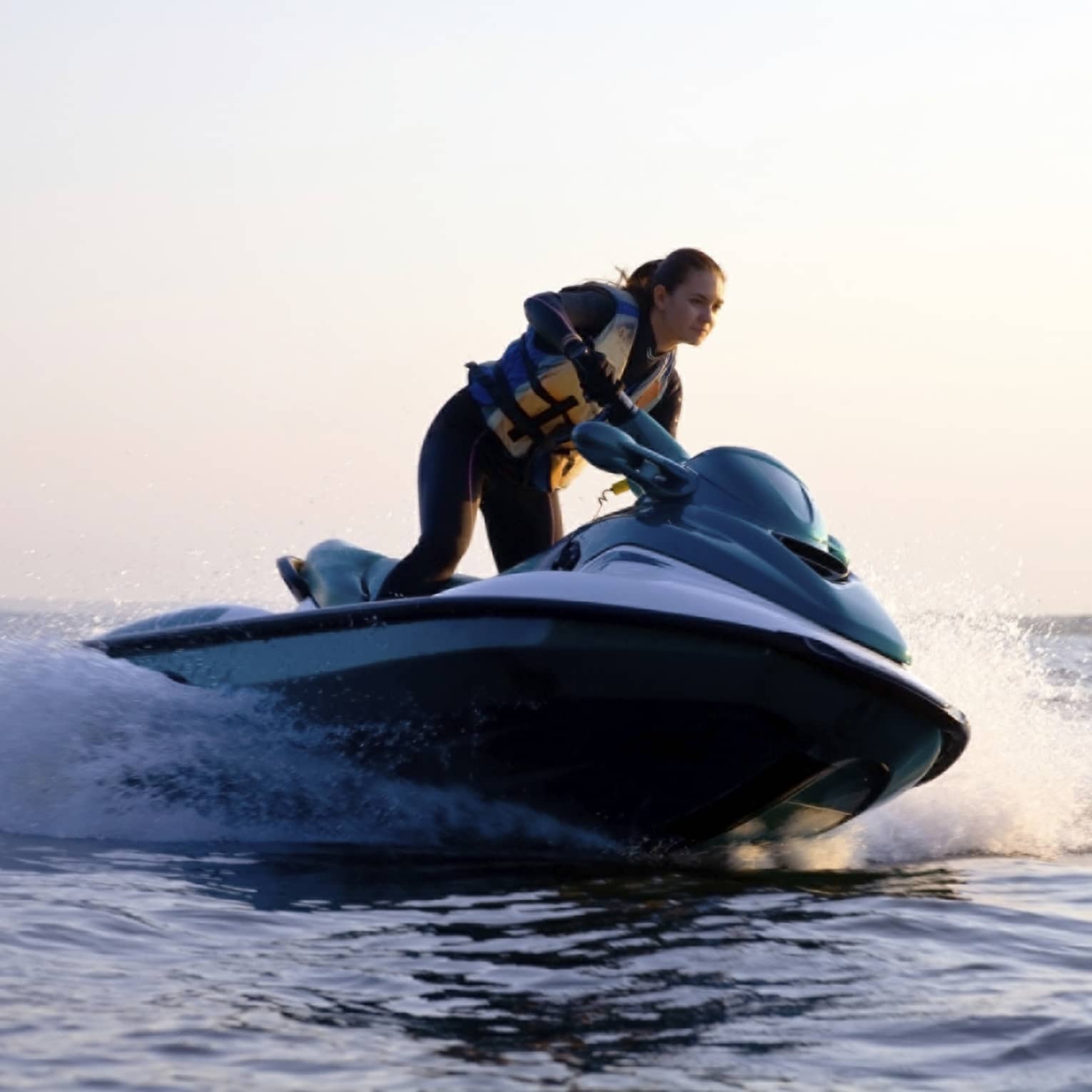 Woman wearing life jacket stands, steers jet ski on ocean at sunset