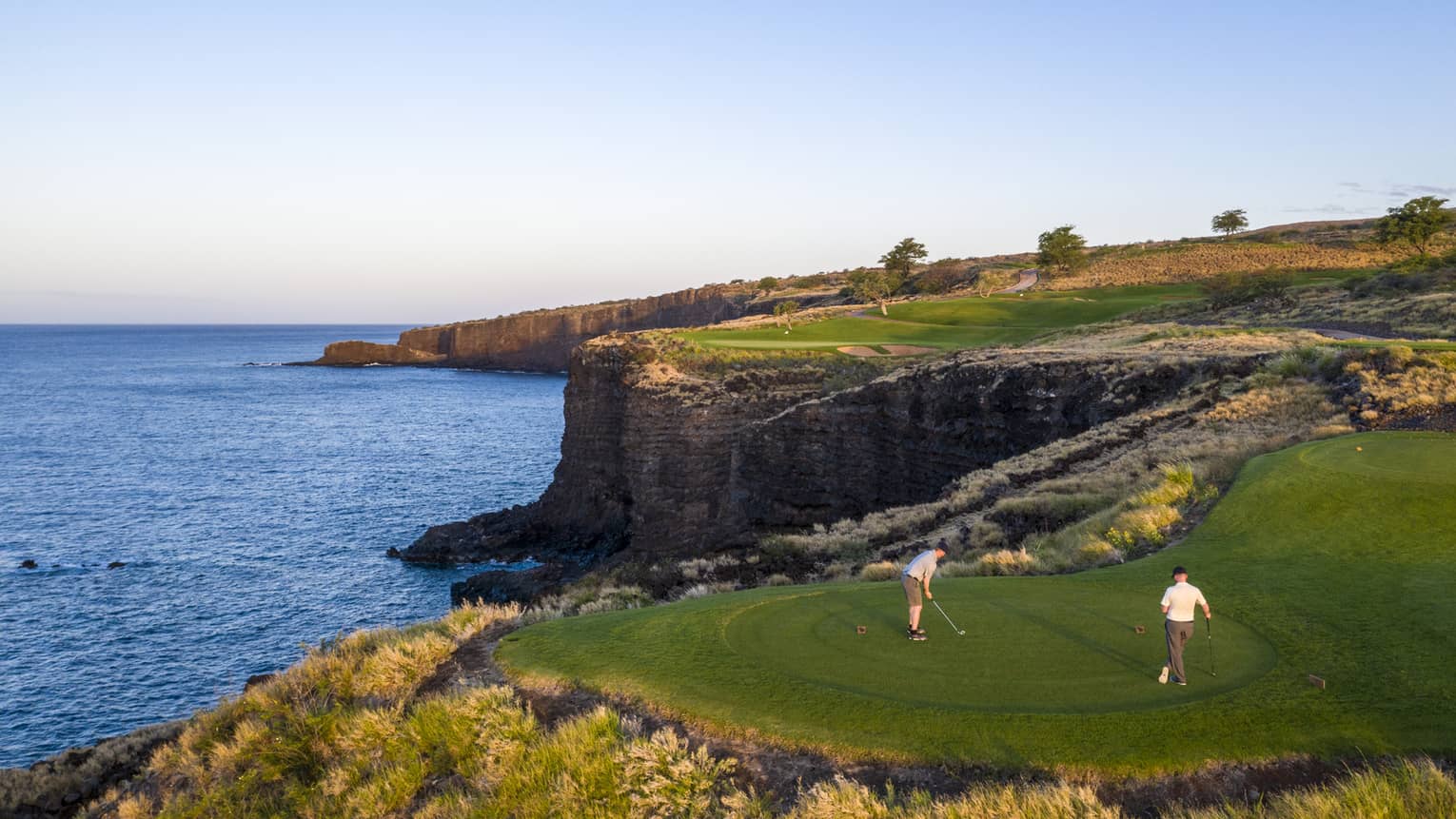 Two golfers at the 12th-hole tee at Manele Golf Course at Four Seasons Resort Lanai, cliffs and ocean in background