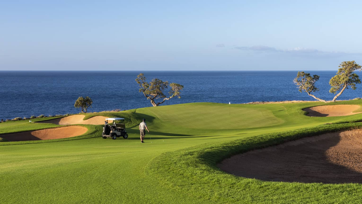 Golfers walk across sweeping green lawn on golf course beside ocean