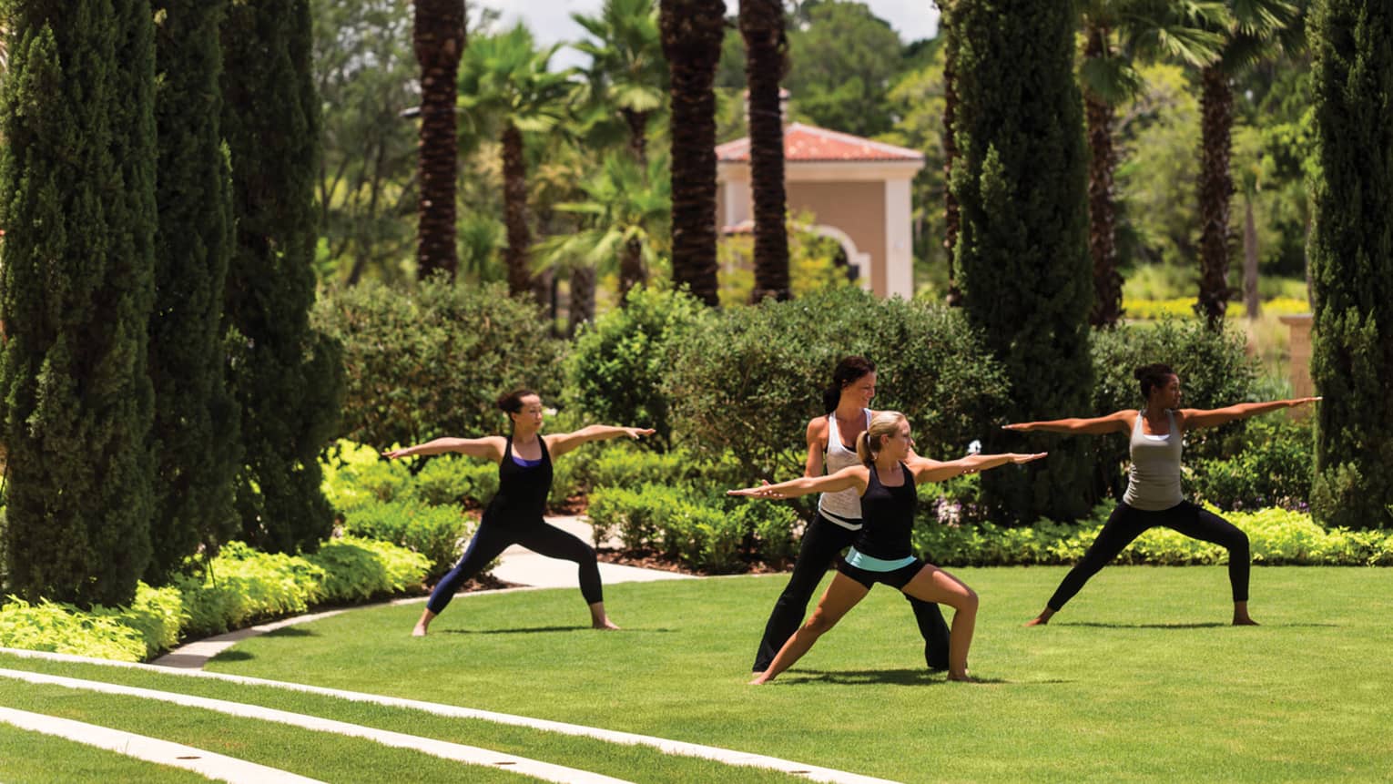 Group of people stand, arms outstretched in yoga poses on green lawn