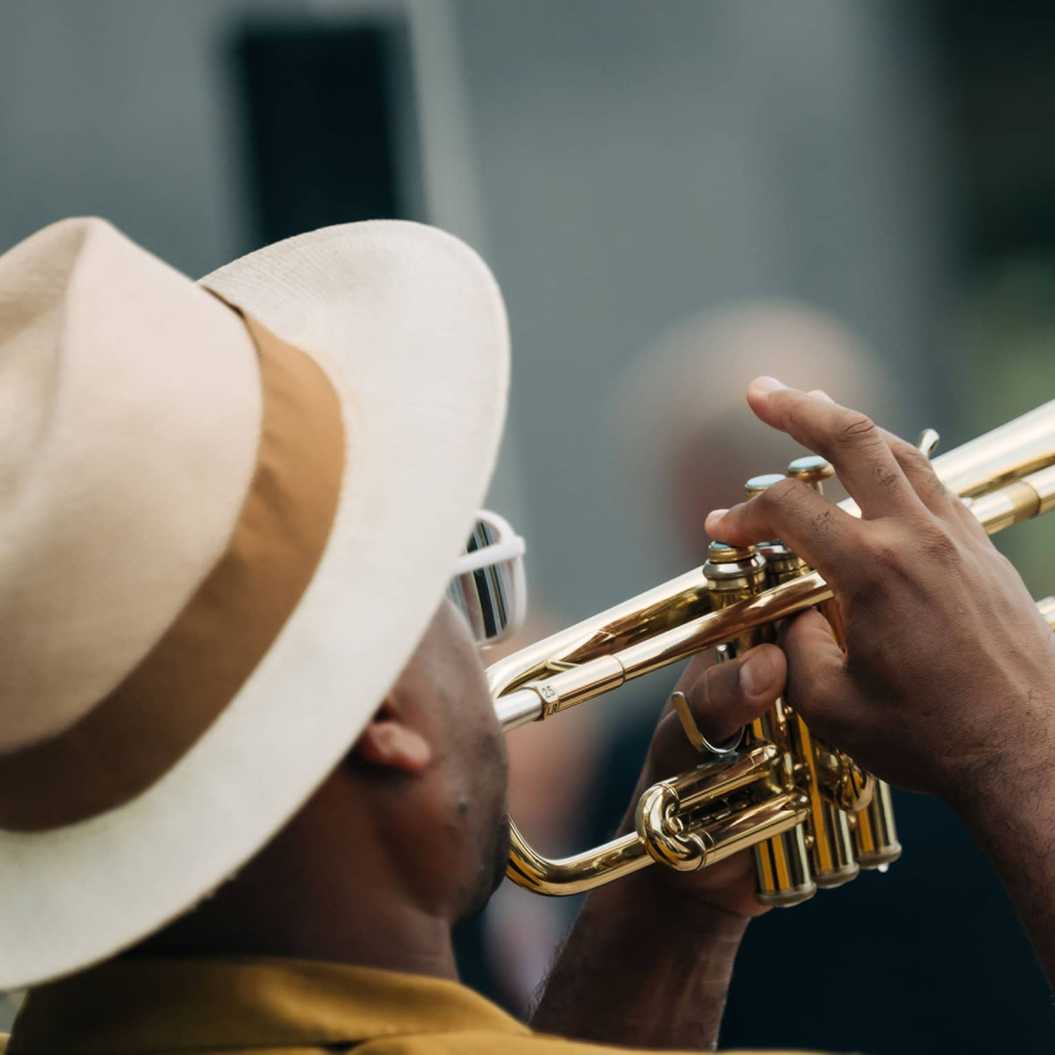 A man wearing a cream-and-taupe fedora with a brown ribbon plays a trumpet