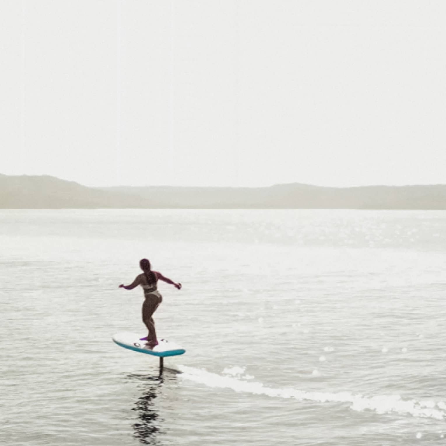 Two silhouetted figues riding e-foil surfboards in the water