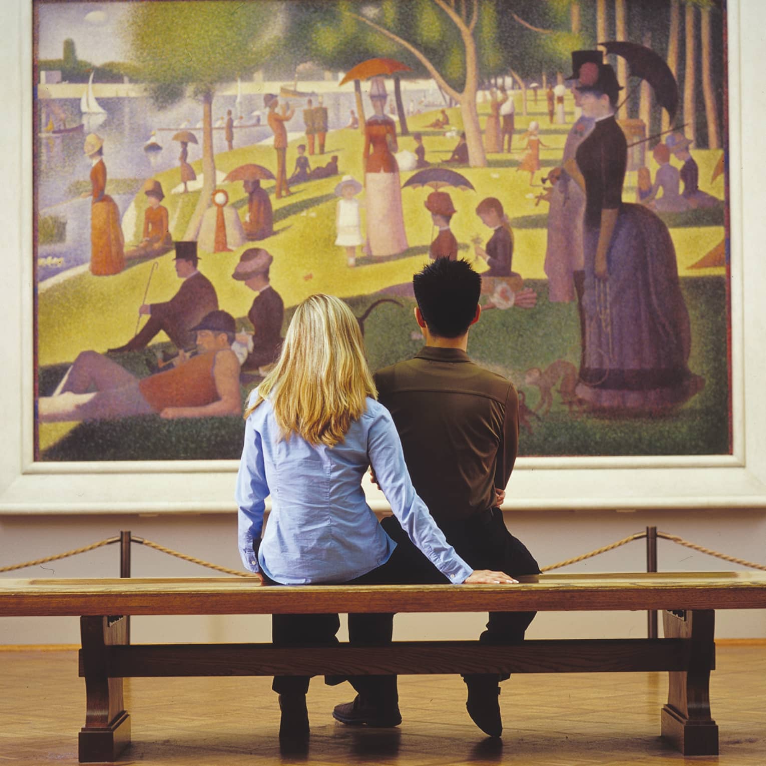 A couple admiring Seurat's iconic Pointillist painting, A Sunday on La Grande Jatte, depicting people strolling in a park.