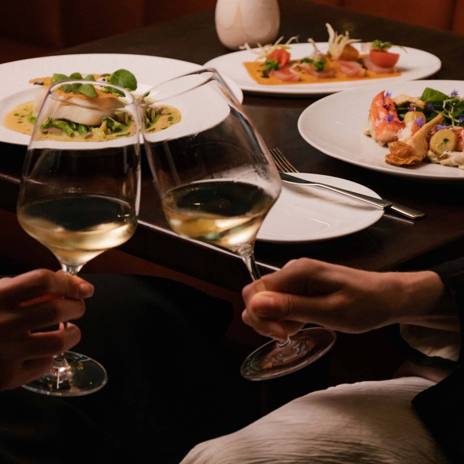 Two people clink glasses of white wine at restaurant table