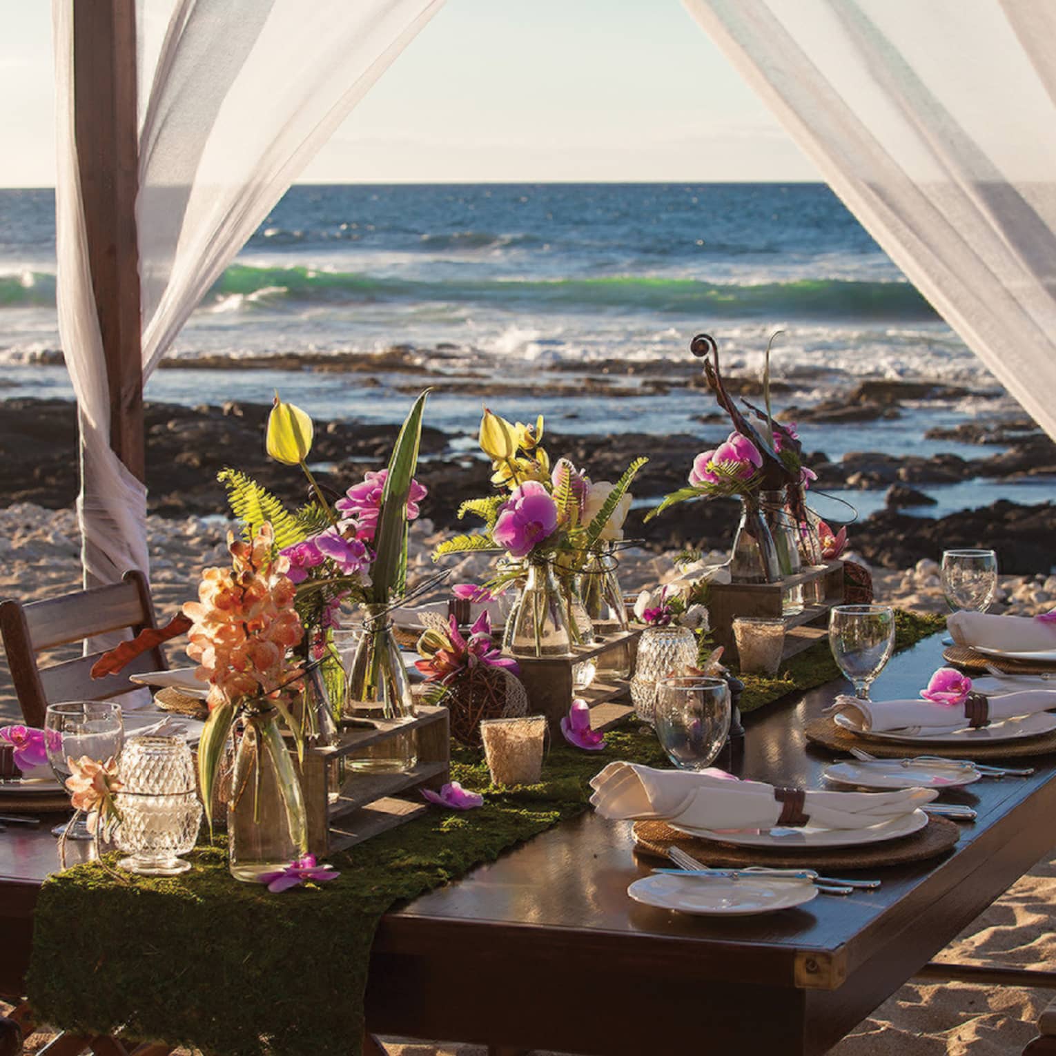 Private beach dining table with floral arrangements and sheer curtains