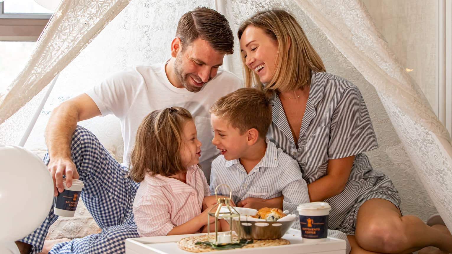 A family under a tent like sheet enjoying coffee.