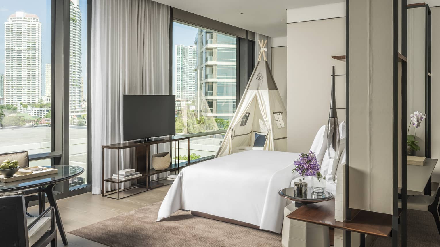 Hotel room with king bed, wall of windows, and kids teepee