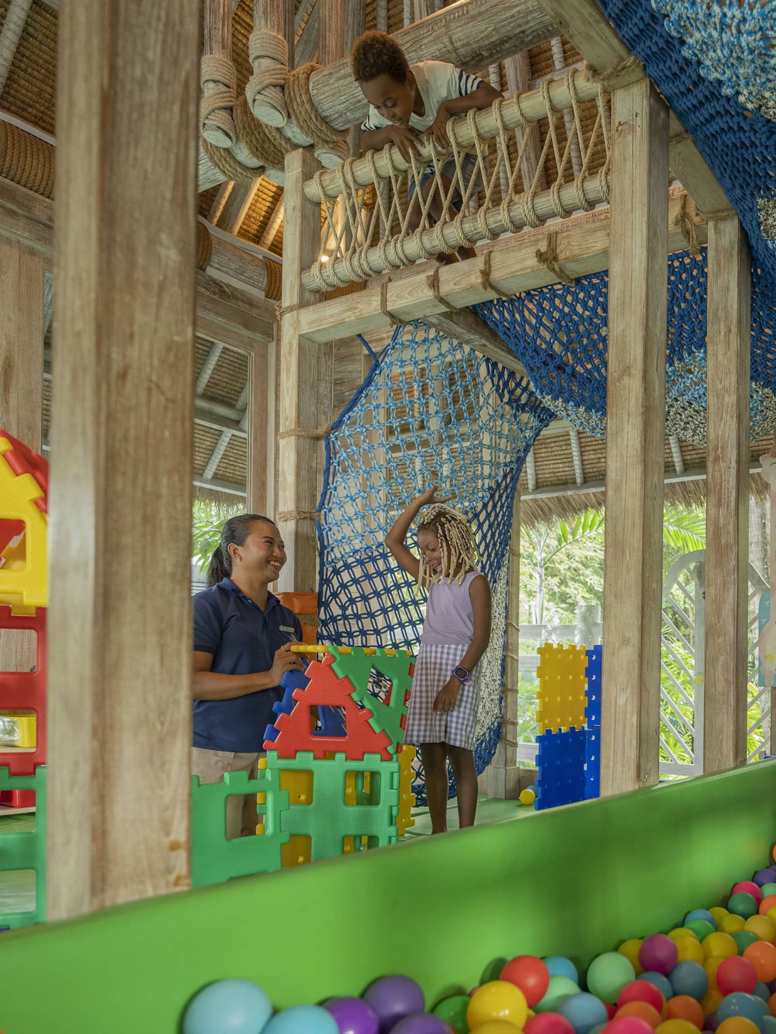 A smiling child building with large colourful blocks with a smiling care worker while in a large colourful indoor playground.