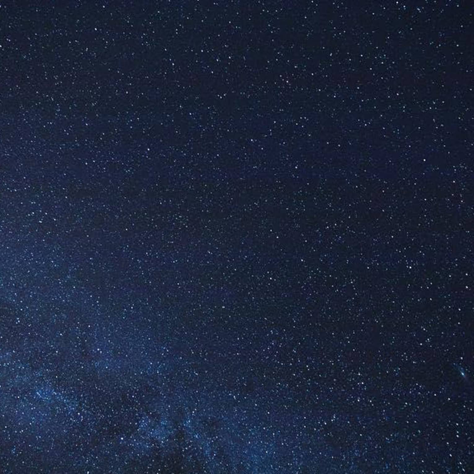 Thousands of stars dusting across a clear night sky; a cluster of stars form the Milky Way, just barely visible in the sky.