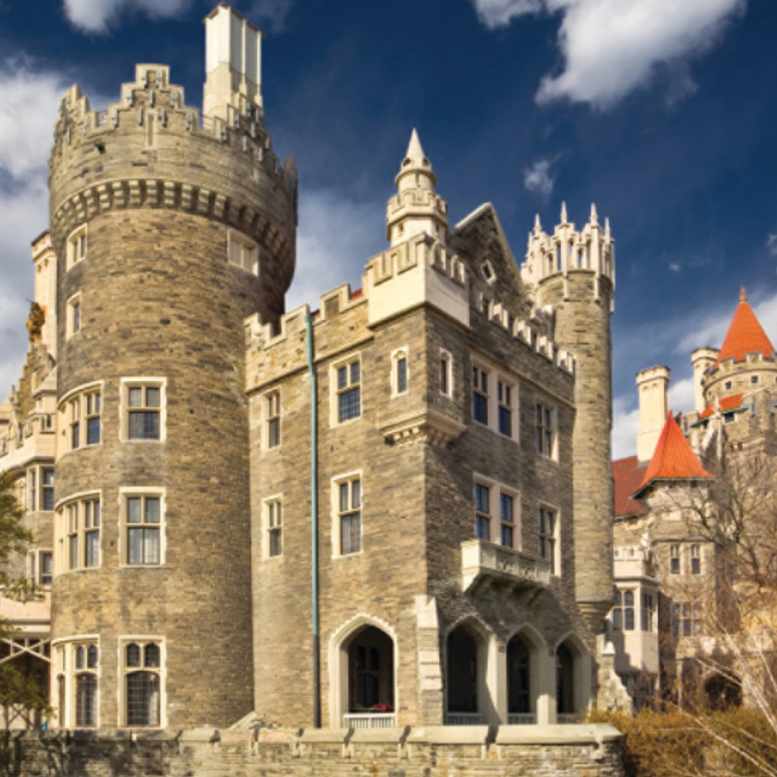 Corner view of a modern sandstone castle adorned with round crenelated towers and red coned roofs under a dark blue sky.