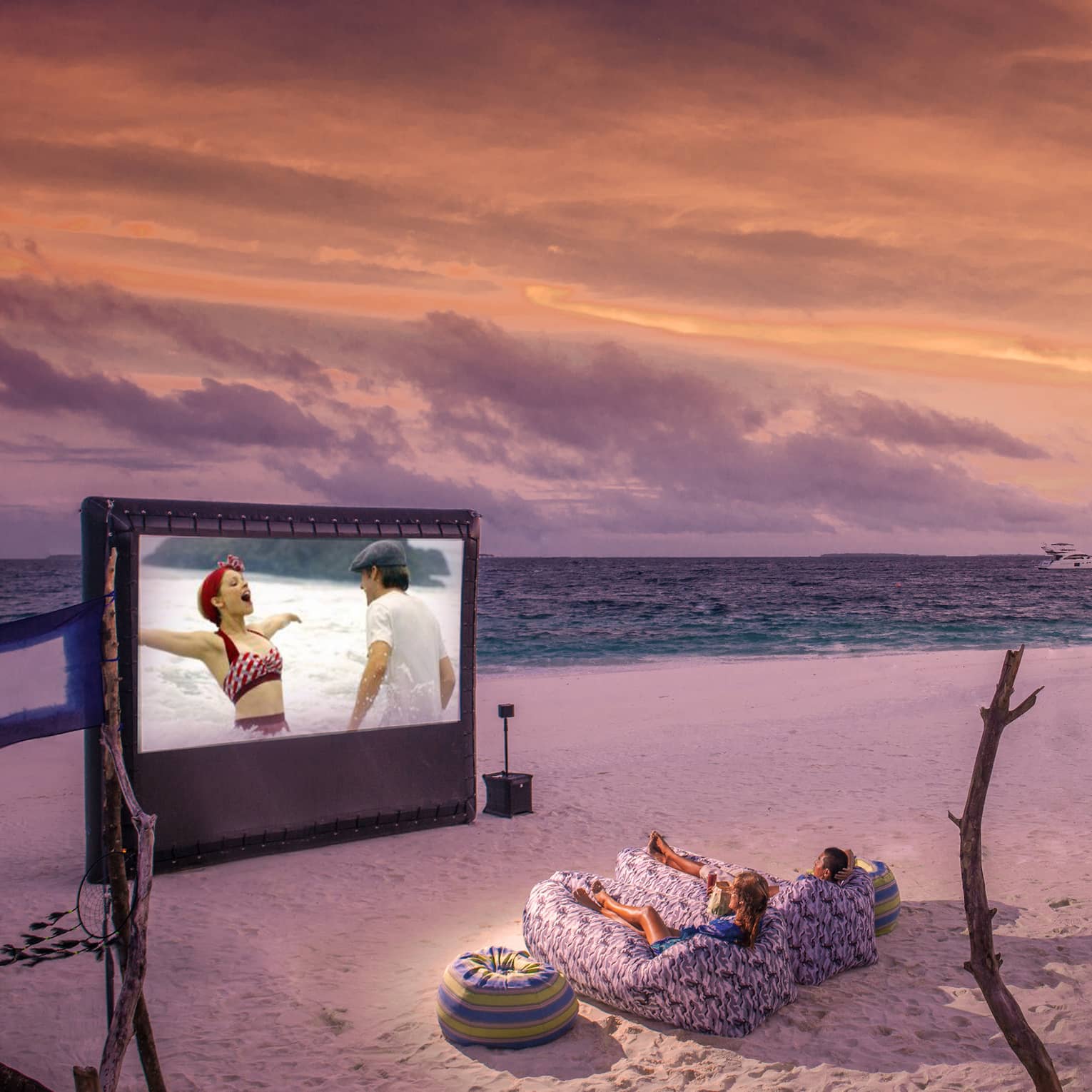 ,Two people in beanbag chairs enjoy a movie night on the beach at dusk, popcorn stand on sand behind them