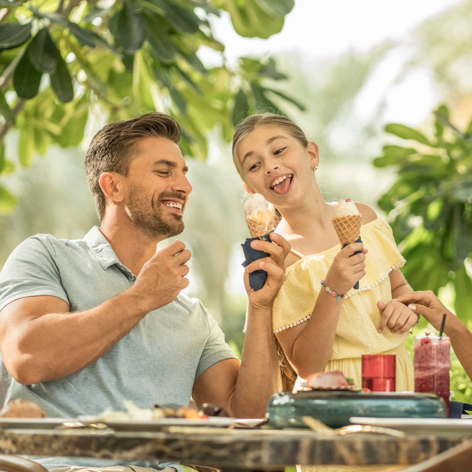 ,A man and young girl eat ice cream cones, while two ladies sitting across from them sip on cocktails