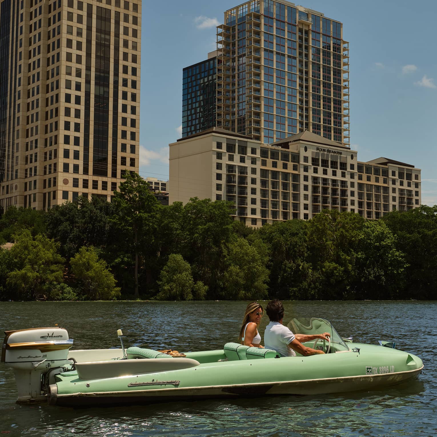 Two guests on a boat in the water with city buildings in the background