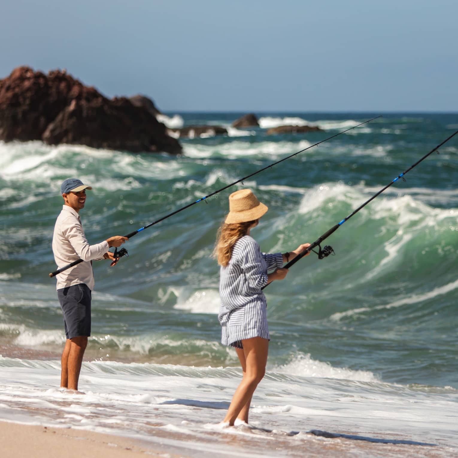 Two people fishing on a beach shore.