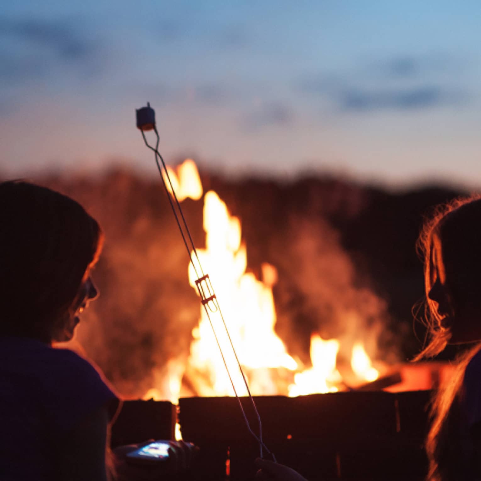 Silhouette of two children roasting marshmallows in front of roaring bonfire