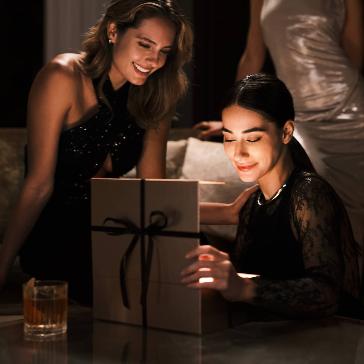 Two guests at a restaurant table smiling while opening a gift.