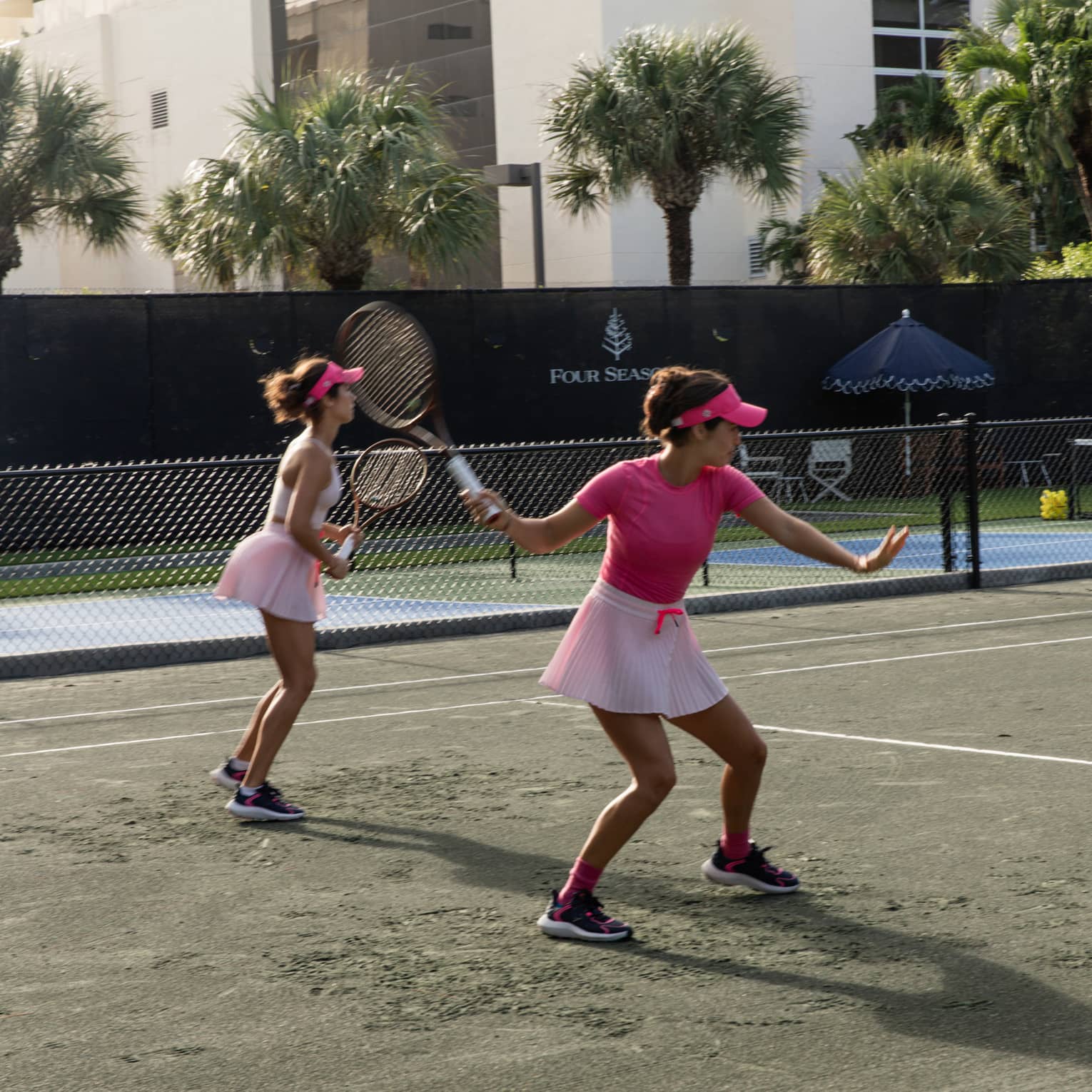 Two tennis players both wearing pink volley on a clay court