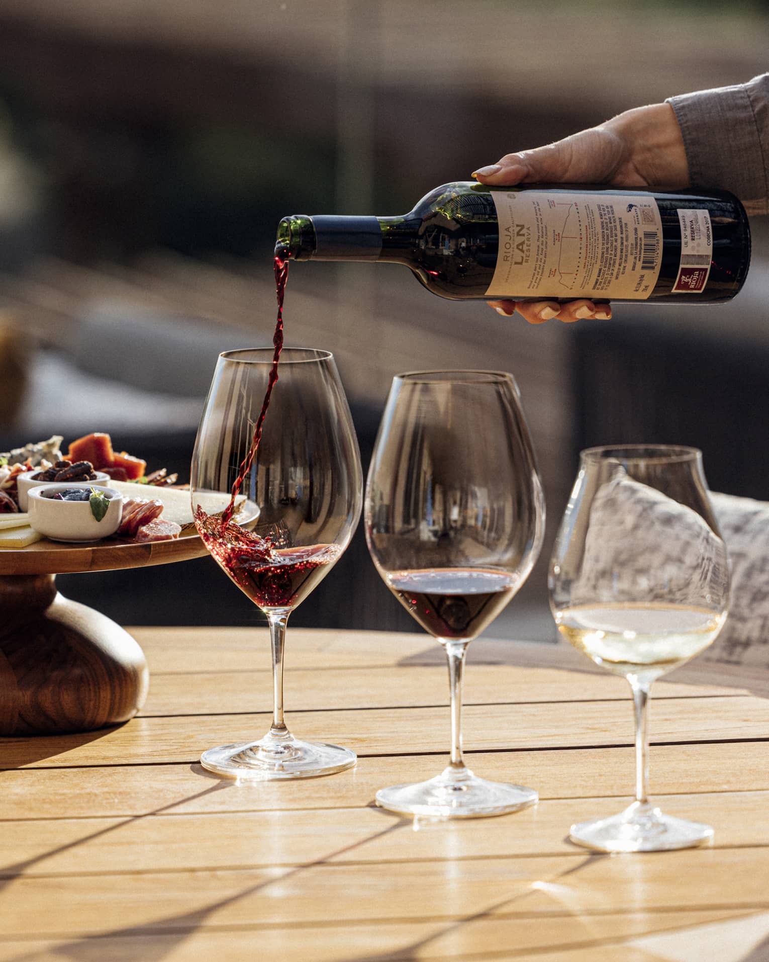 Three glasses of wine are poured next to a plate of charcuterie