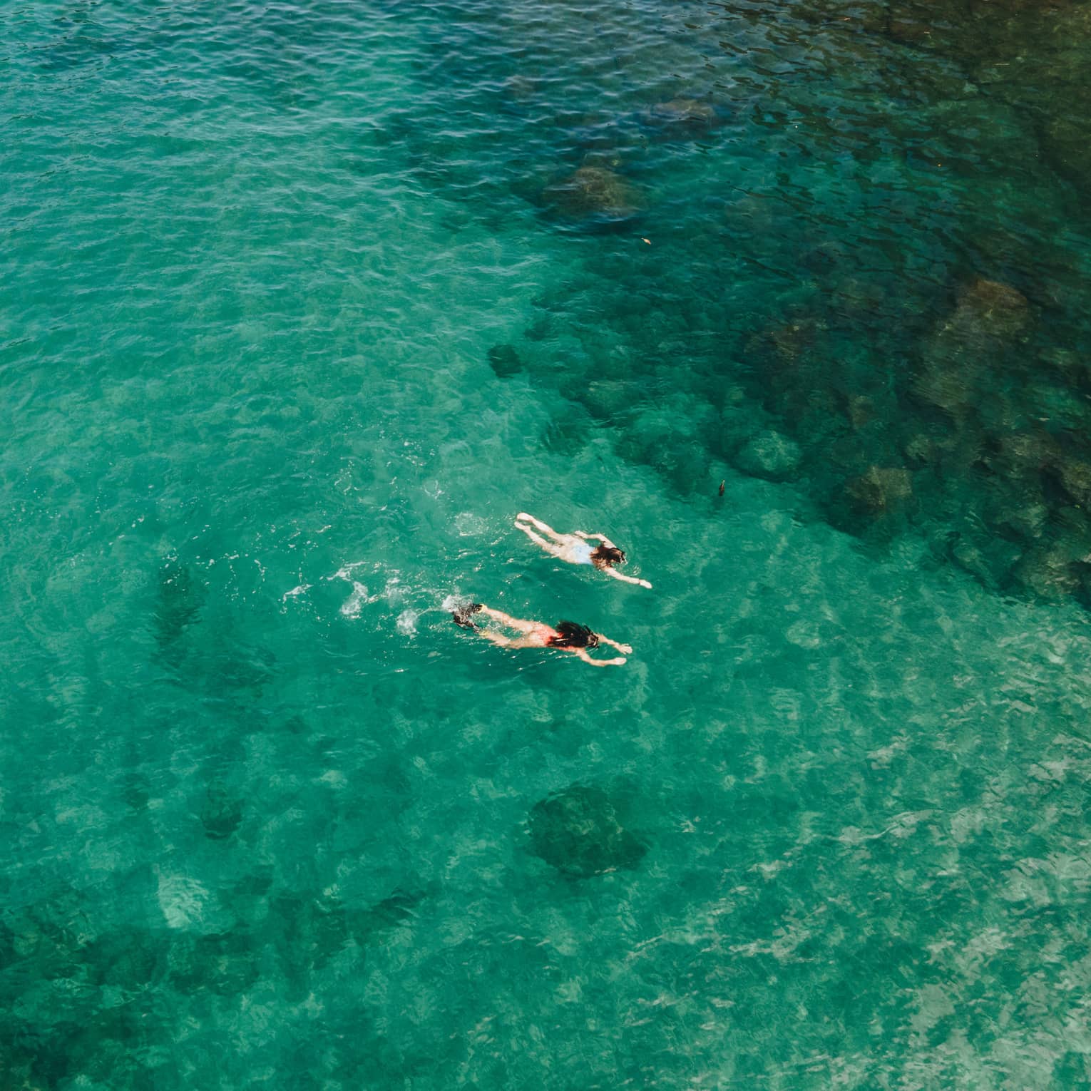 Aerial view of two people snorkelling through blue-green water