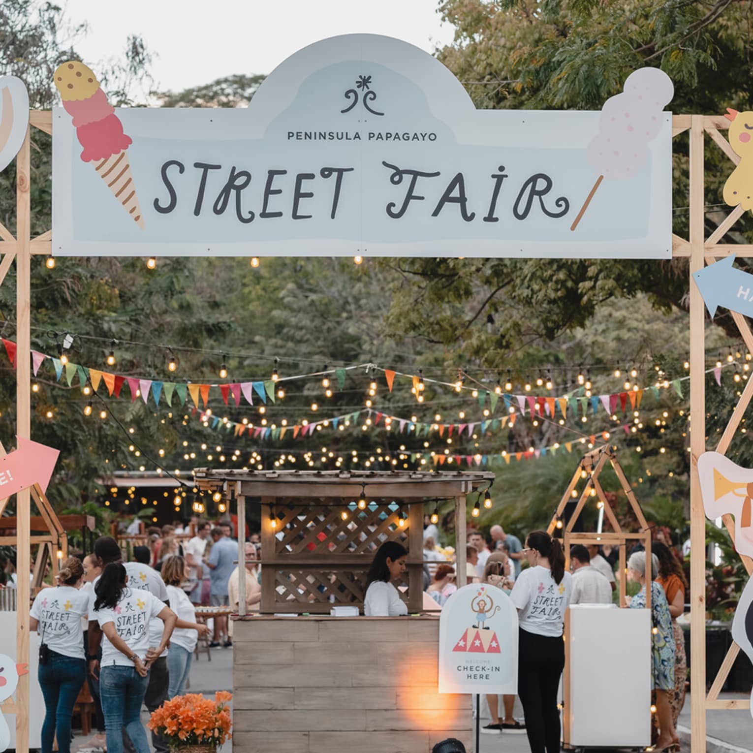 A colorful archway with a sign that reads "Street Fair" serves as an entrance to a street decorated with sting lights, multi-color pendant banners and booths