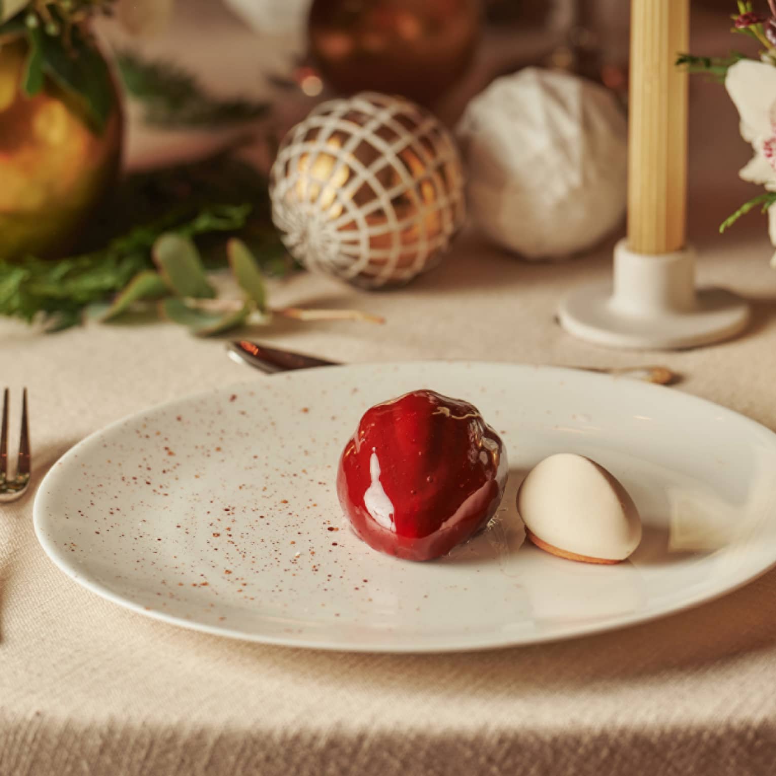 Modern, glossy, red ice cream dessert on a plate, with festive ornaments as decoration on the table