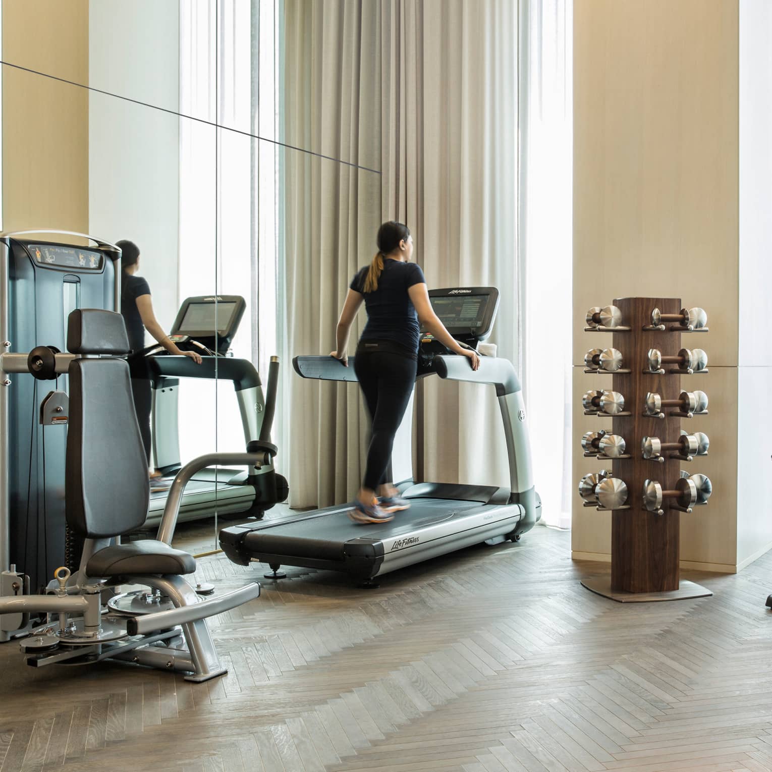 Woman walks on treadmill beside mirror wall