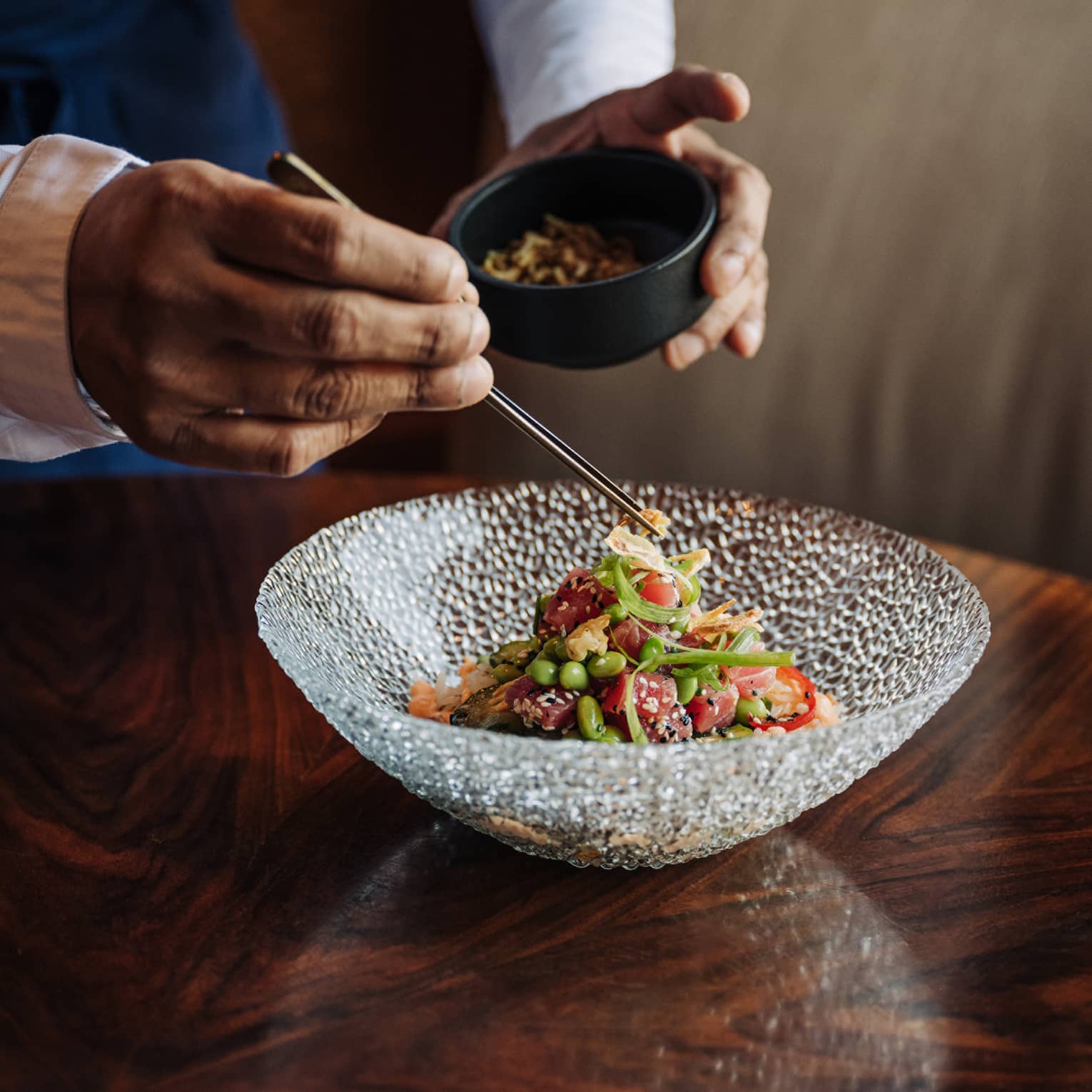 Waiter uses chopsticks to place item on top of salad in a clear glass bowl