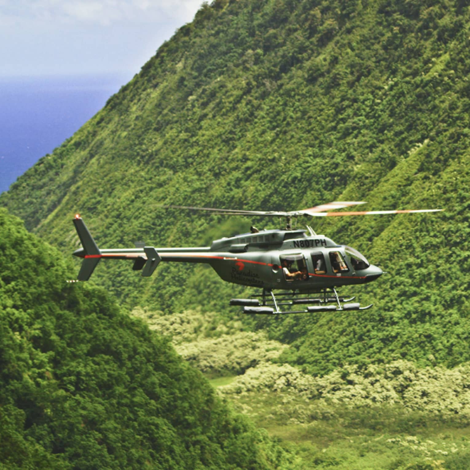 Orange and grey helicopter flying through crevice between green mountains
