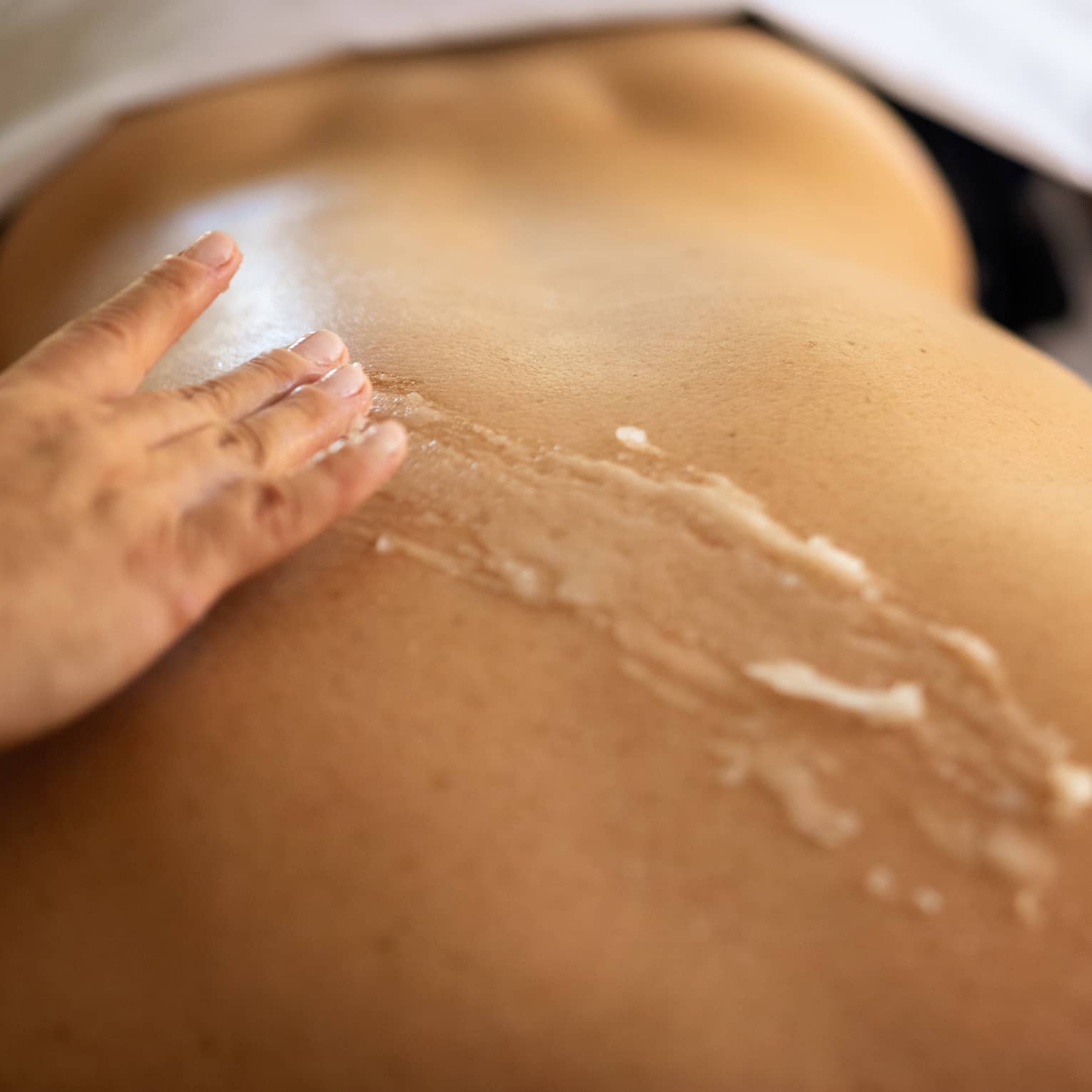 A therapist applies scrub to a person's back during spa treatment