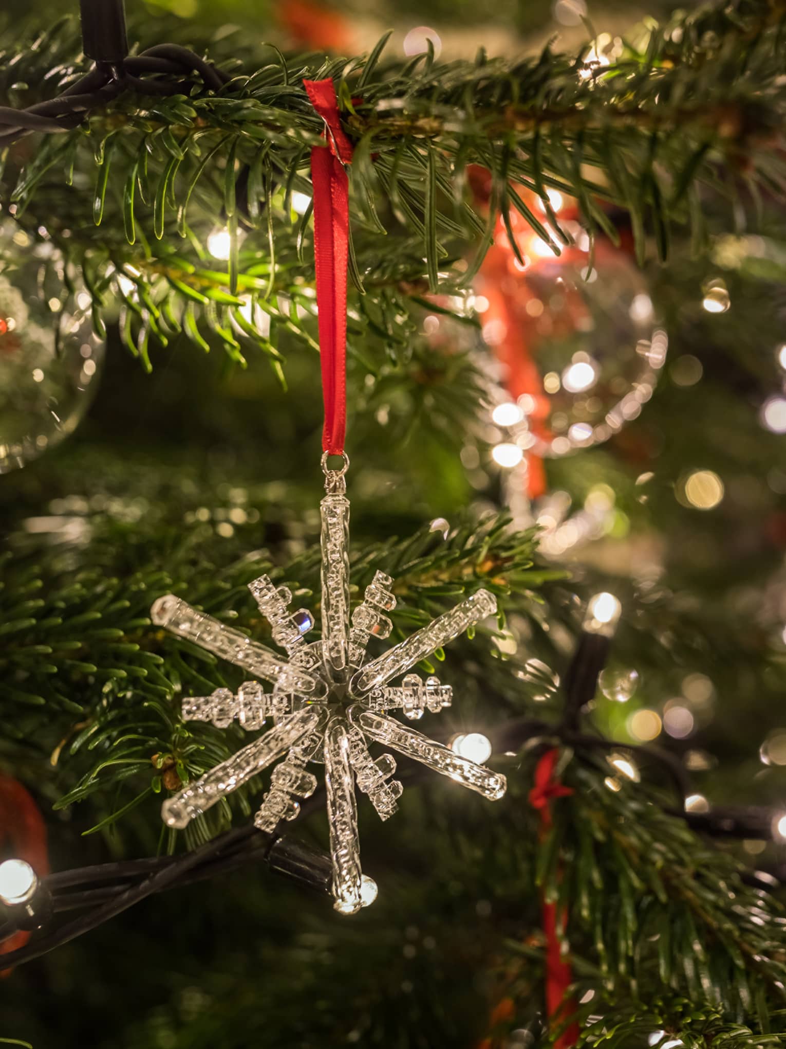Close-up of a crystal snowflake ornament hanging on a Christmas tree with festive lights in the background