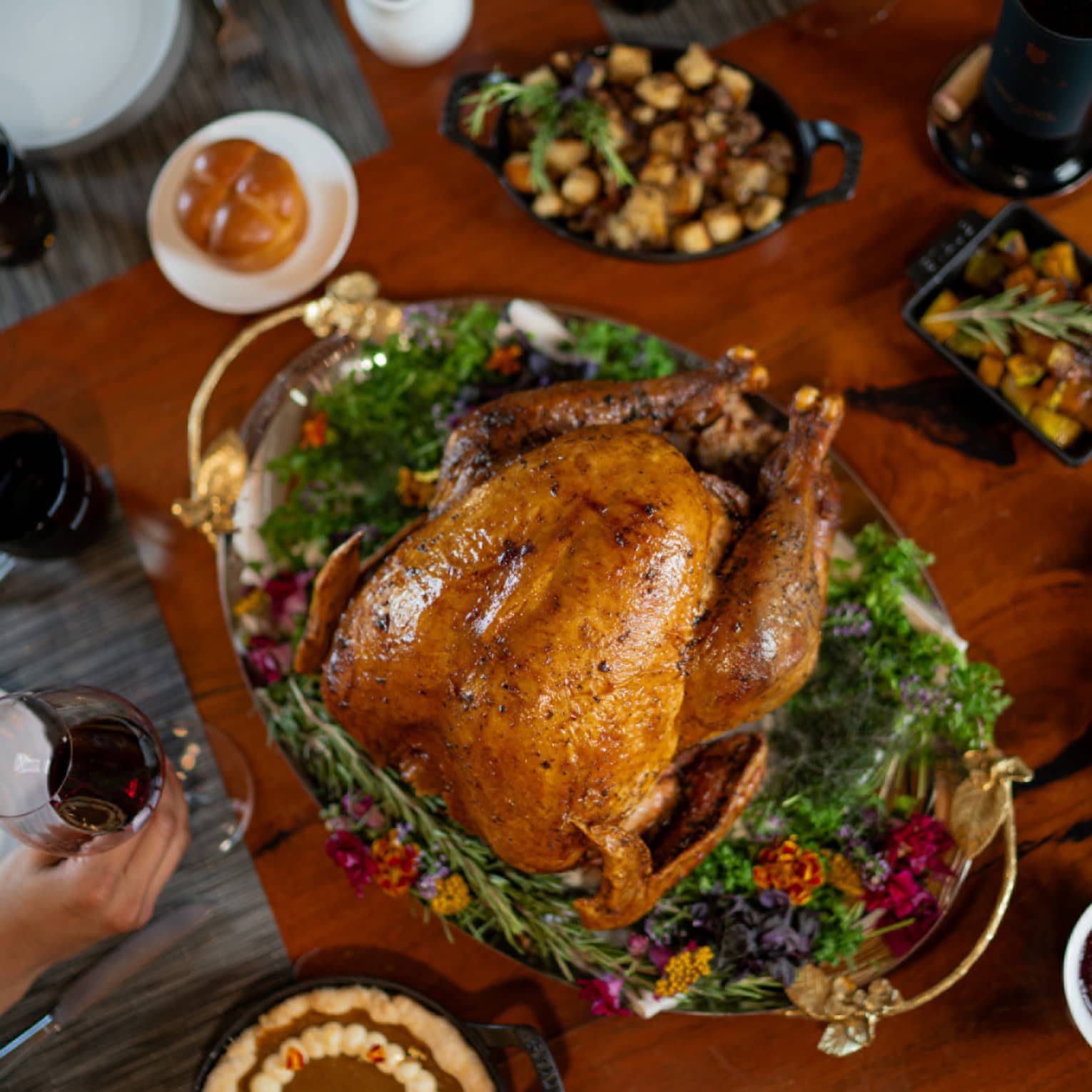 A table with a cooked turkey and Thanksgiving sides around it.