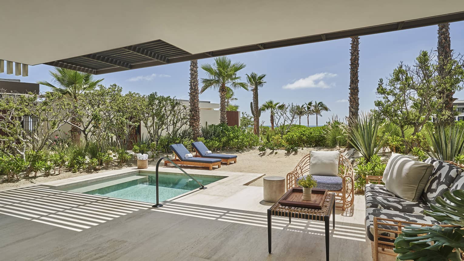 An outdoor area with sofa, chair, lounge chairs and plunge pool.