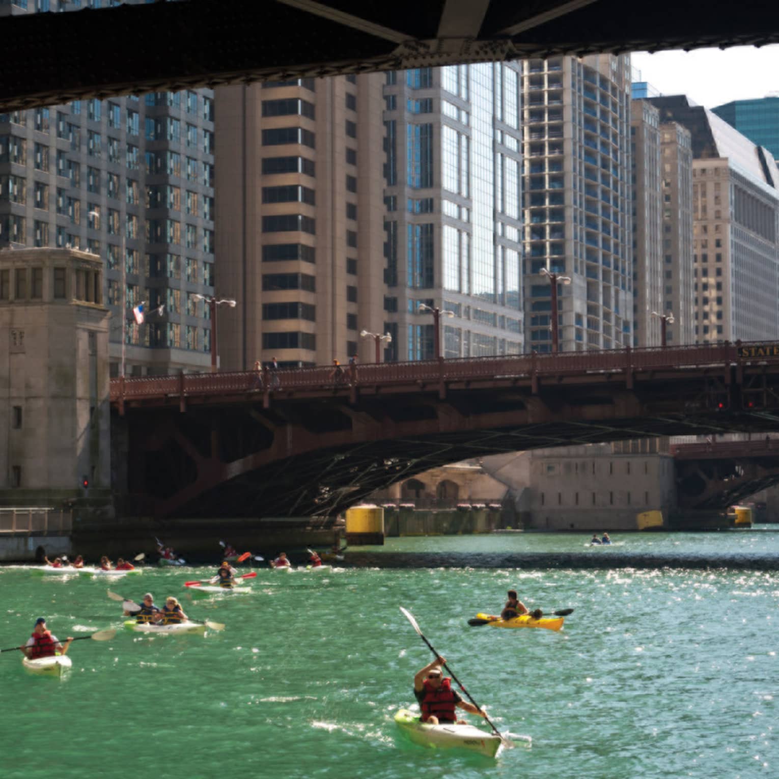 People kayaking on a river under a bridge.