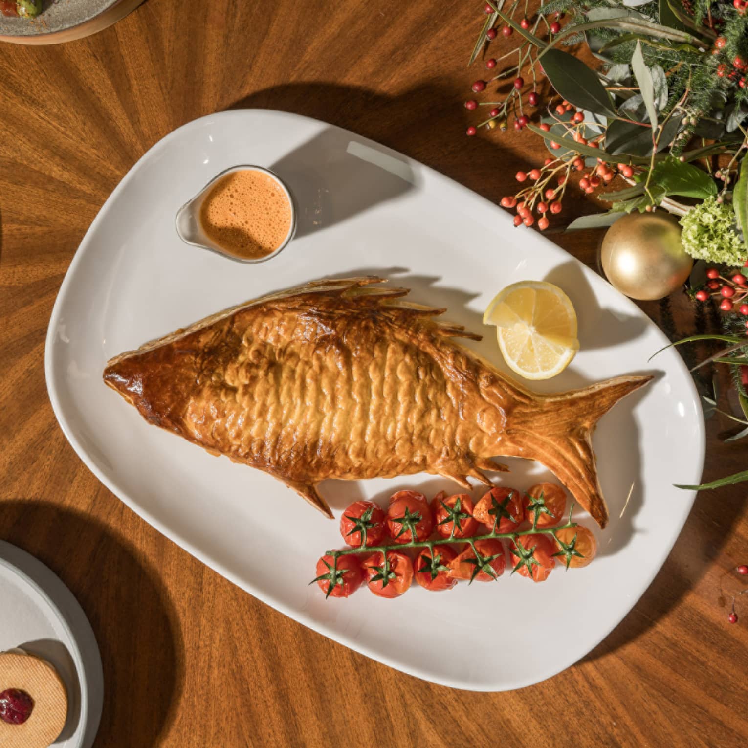 Whole crusted fish served on a white plate next to festive decorations