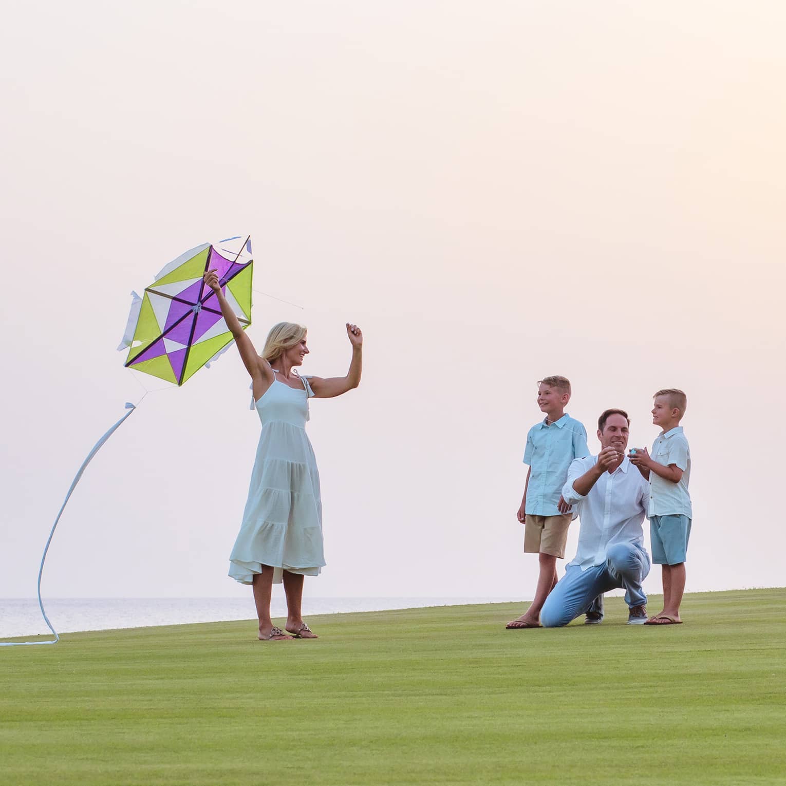 A family about to fly a kite while resting on green grass.