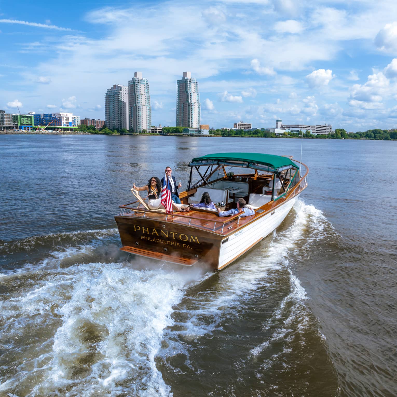 Guests on a boat in the water with city buildings in the background.
