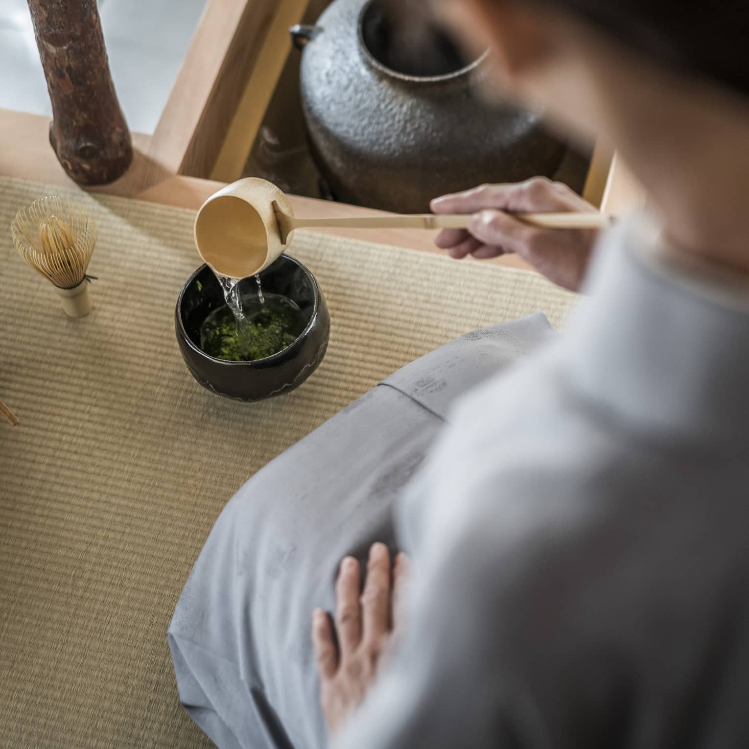 Woman kneels and pours tea from ladle during Tea Ceremony