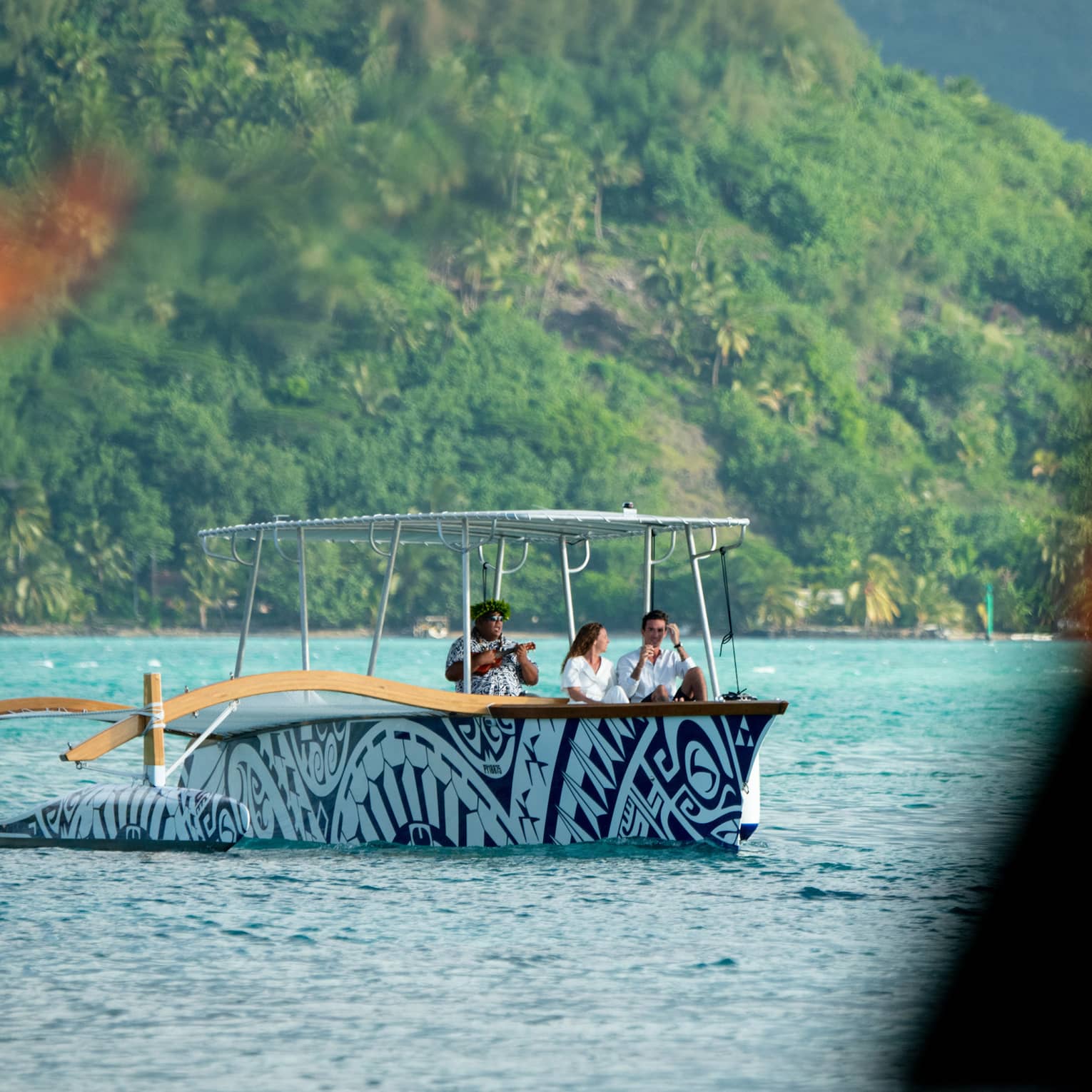 A motorized outrider canoe carries a couple and a musician across the ocean; in the foreground torches flicker with fire.