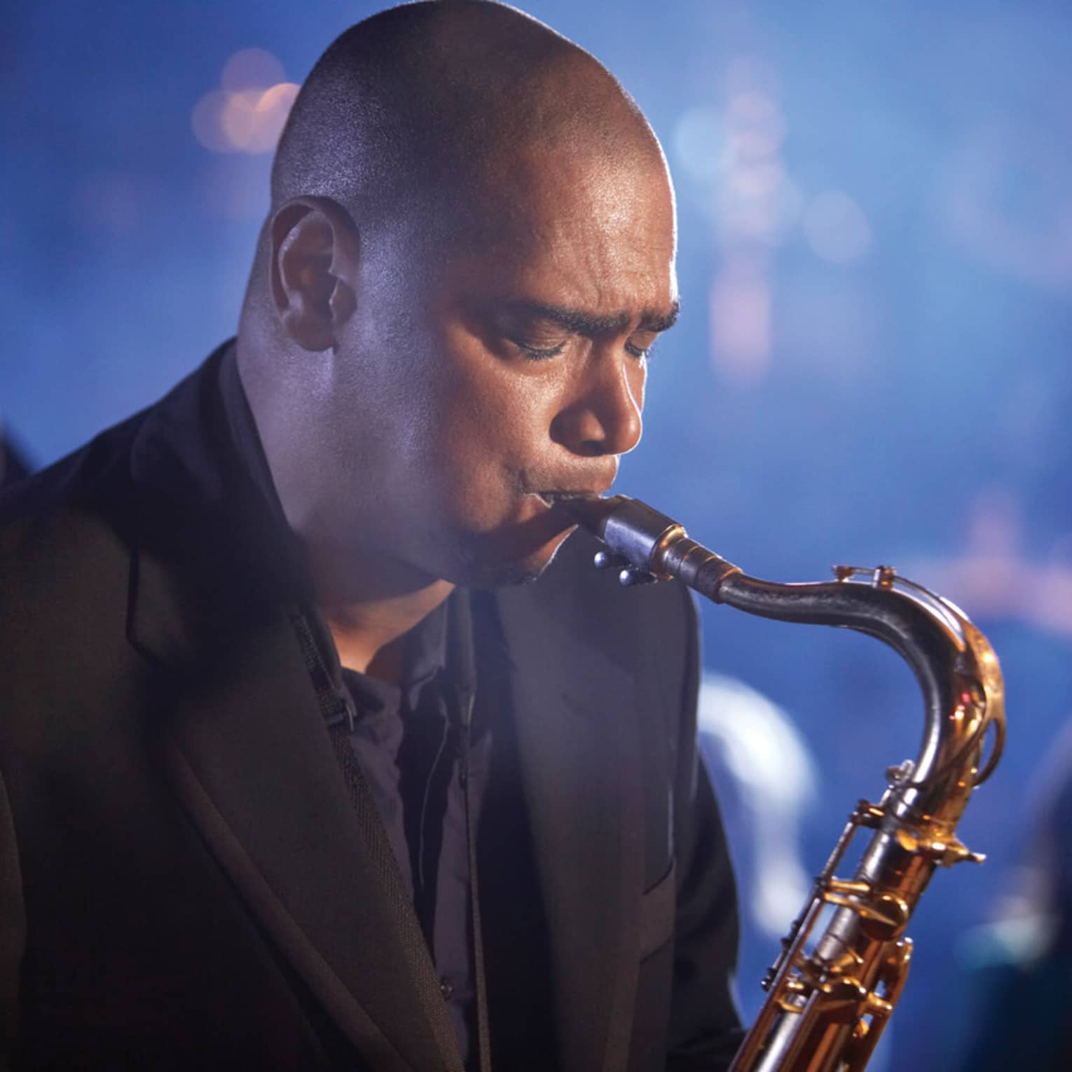 A close up of a man with his eyes closed, playing a saxaphone at a Jazz club in Ten Trinity